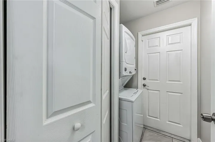 Washroom featuring stacked washer / drying machine and light tile patterned floors