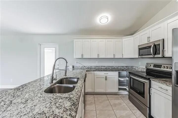 Kitchen with stainless steel appliances, white cabinets, sink, light stone counters, and light tile patterned floors