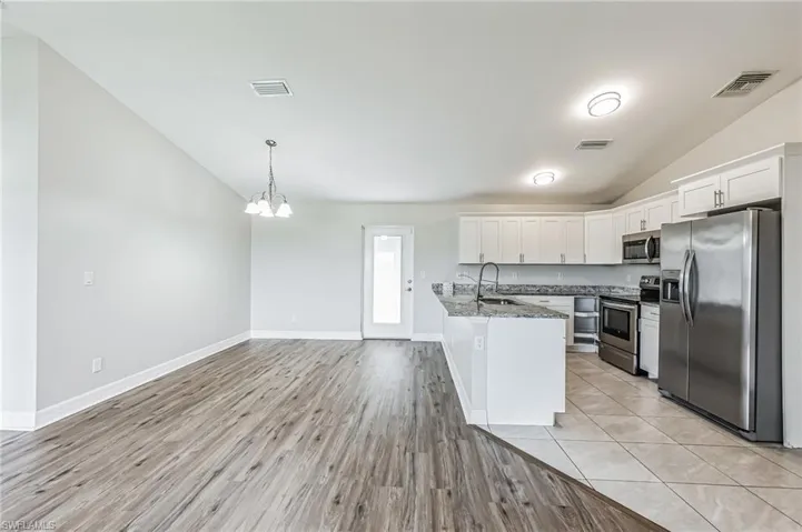 Kitchen featuring white cabinetry, light wood-type flooring, stainless steel appliances, vaulted ceiling, and sink