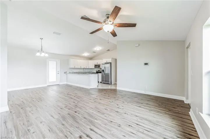 Unfurnished living room with lofted ceiling, ceiling fan with notable chandelier, hardwood / wood-style floors, and sink