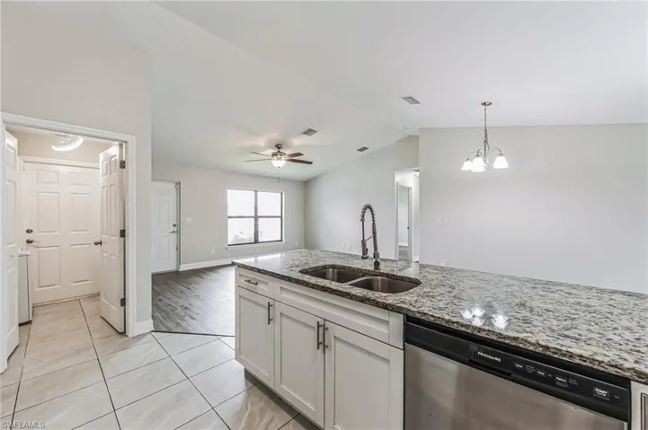 Kitchen featuring sink, light stone counters, light tile patterned floors, ceiling fan with notable chandelier, and dishwasher