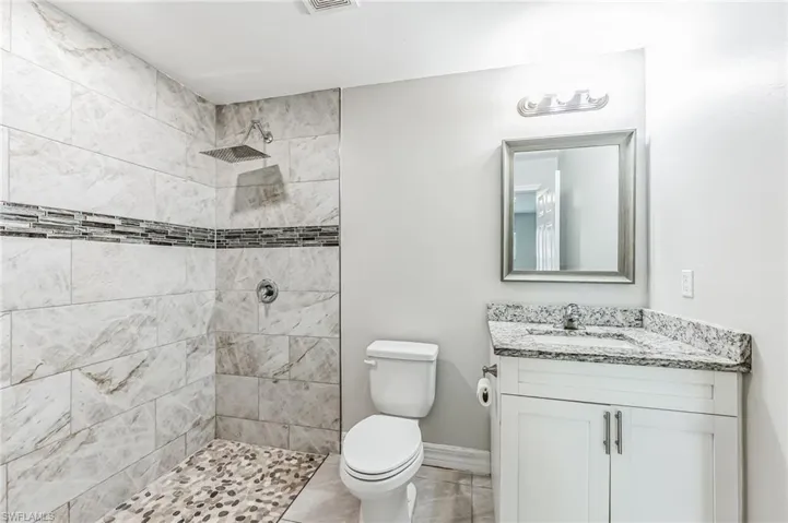 Bathroom featuring vanity, toilet, a tile shower, and tile patterned flooring