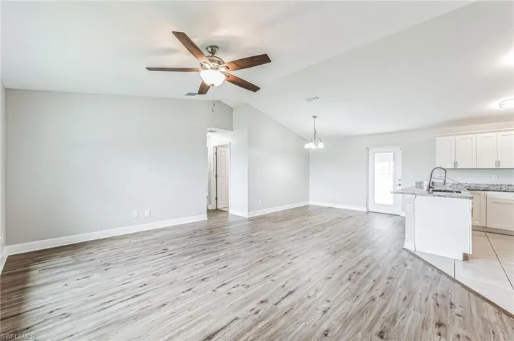 Unfurnished living room with sink, light wood-type flooring, ceiling fan with notable chandelier, and vaulted ceiling