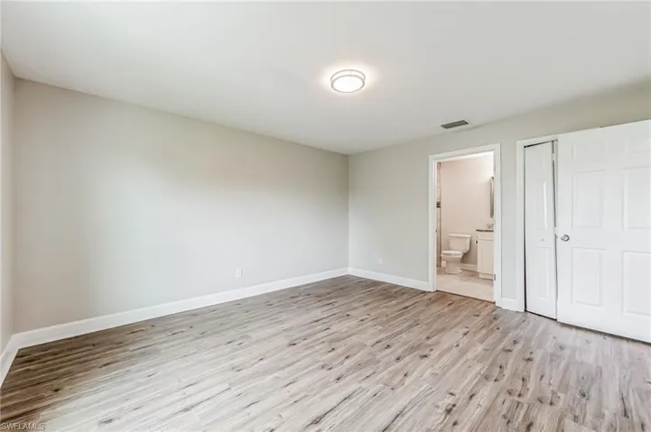Unfurnished bedroom featuring a closet, ensuite bath, and light wood-type flooring