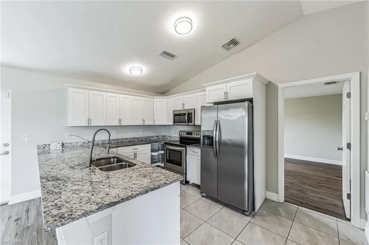 Kitchen with white cabinets, sink, vaulted ceiling, appliances with stainless steel finishes, and light hardwood / wood-style flooring