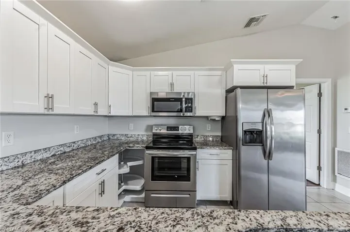 Kitchen with white cabinets, lofted ceiling, light tile patterned flooring, and appliances with stainless steel finishes