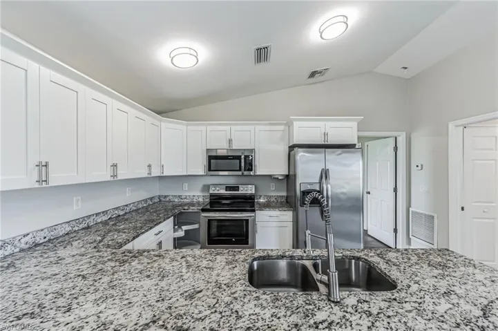 Kitchen with stainless steel appliances, vaulted ceiling, white cabinets, sink, and light stone counters