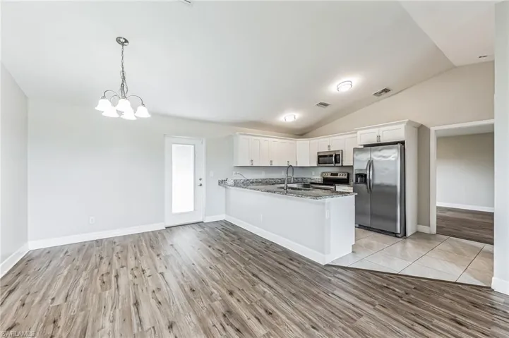 Kitchen featuring stainless steel appliances, kitchen peninsula, light hardwood / wood-style floors, lofted ceiling, and white cabinetry
