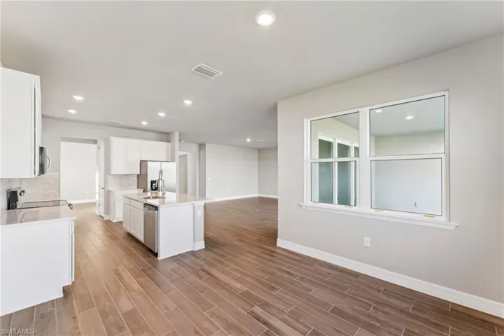 Kitchen with stainless steel appliances, tasteful backsplash, light hardwood / wood-style floors, white cabinets, and a center island with sink