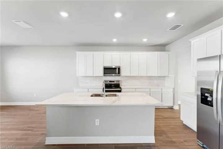 Kitchen featuring stainless steel appliances, a center island with sink, and white cabinets