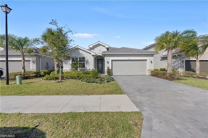 Single-story residence featuring a gray exterior, stone facade accents, an attached two-car garage, mature palm trees, and a paver driveway
