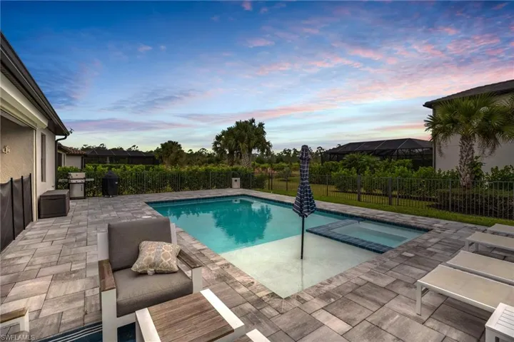 Pool at dusk featuring a patio, a fenced backyard, a grill, and a pool with connected hot tub
