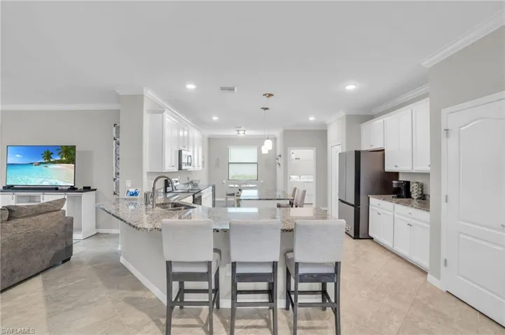 Kitchen with light stone countertops, a peninsula, crown molding, white cabinetry, and recessed lighting