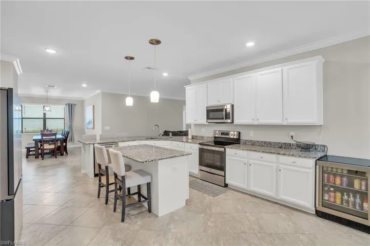 Kitchen featuring white cabinets, appliances with stainless steel finishes, decorative light fixtures, a breakfast bar, and beverage cooler