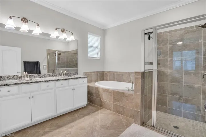 Full bath with a bath, ornamental molding, a stall shower, double vanity, and light tile patterned floors