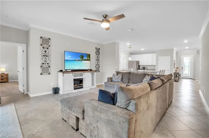 Living room featuring crown molding, a glass covered fireplace, ceiling fan, light tile patterned floors, and recessed lighting