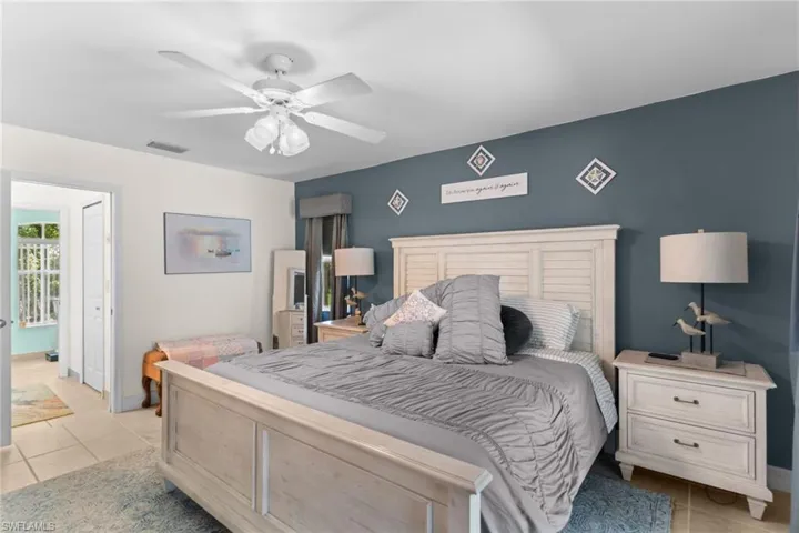 Bedroom featuring a light-toned wood-finish bed frame and headboard, ceiling fan, and tile flooring