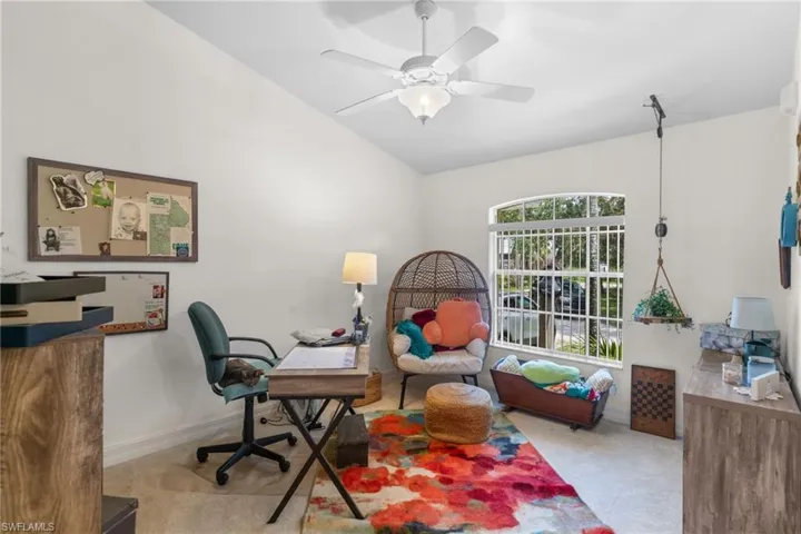 Spacious room featuring vaulted ceilings, a ceiling fan with integrated lighting, a large arched window with horizontal blinds, and neutral-toned wall paint
