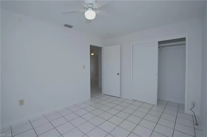 This room features white tile flooring, a ceiling fan with integrated lighting, and a closet with sliding doors