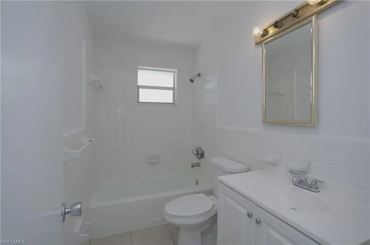 The bathroom features a vanity with a white countertop and cabinet, a toilet, and a bathtub with white tiled walls and a window