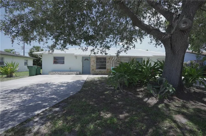 The property features a light-colored exterior with stone accents, a prominent front tree, and a concrete driveway