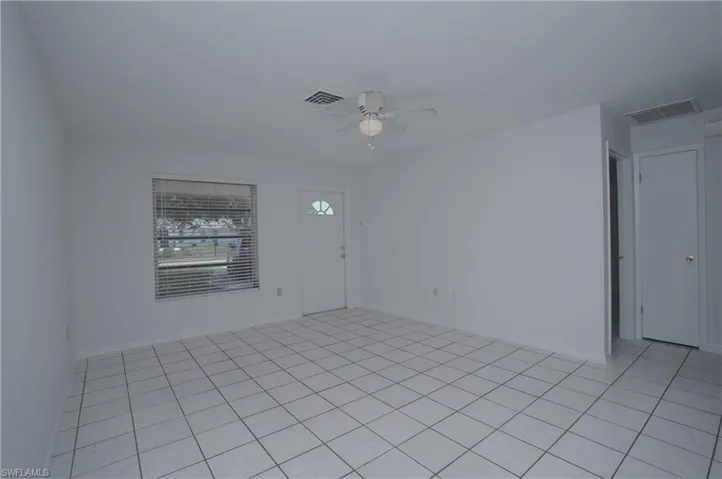 This open concept living area features white tile flooring, a window with horizontal blinds, and a ceiling fan with integrated lighting