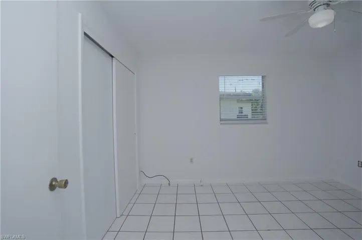 This room features white tile flooring, a window with horizontal blinds, and a ceiling fan with an integrated light fixture