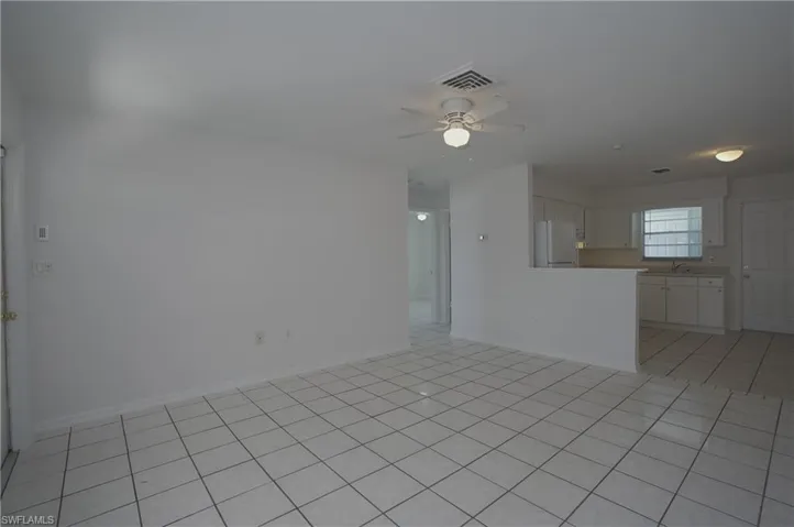Spacious living area featuring light-colored tile flooring, a ceiling fan, and an open layout connecting to the kitchen area