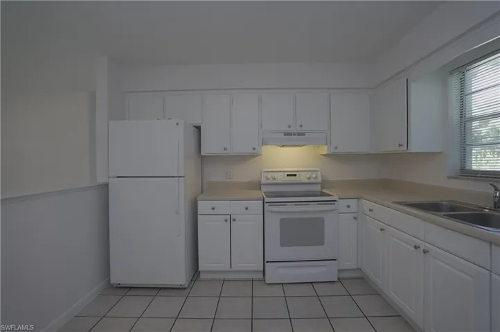 The kitchen features white cabinetry, a white refrigerator, a white electric range, and a double basin sink
