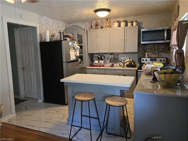 Kitchen with light marble finish flooring, gray cabinets, stainless steel appliances, a breakfast bar, and a textured ceiling