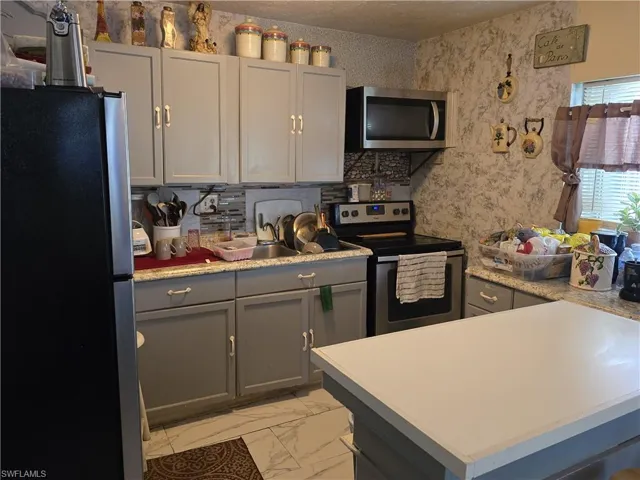 Kitchen with stainless steel appliances, gray cabinetry, light marble finish floors, light countertops, and wallpapered walls