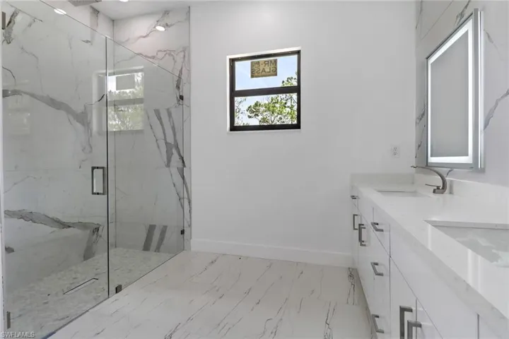 Bathroom featuring a marble finish shower, double vanity, and marble look tile flooring