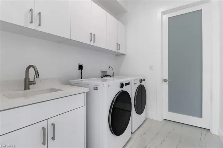 Laundry room featuring cabinet space, washing machine and clothes dryer, and light marble finish flooring