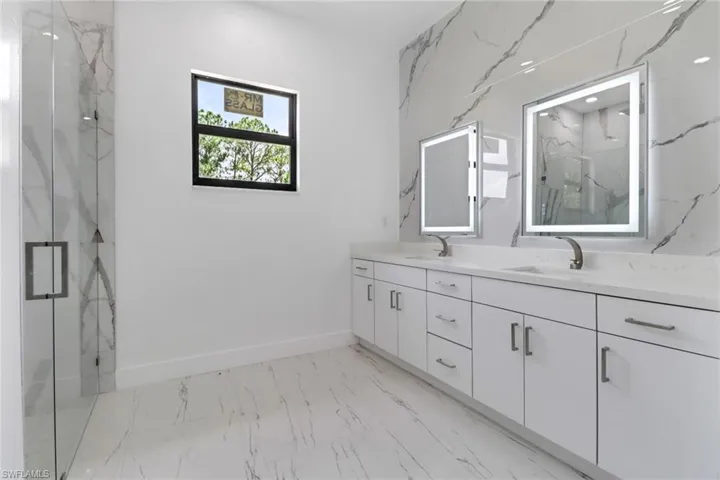Bathroom with double vanity, a marble finish shower, and marble finish floors