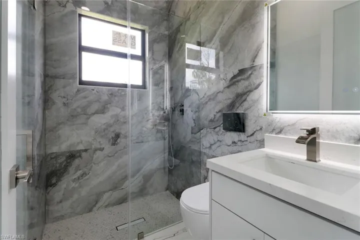 Bathroom with vanity, a marble finish shower, marble look tile flooring, and tile walls