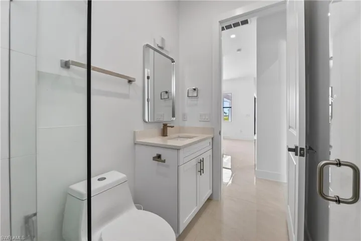 Contemporary bathroom featuring a frameless glass shower enclosure, a single vanity with stone countertop, and a sleek rectangular mirror