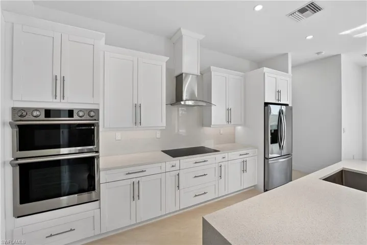 Bright kitchen featuring white shaker cabinetry, stainless steel appliances, a built-in double oven, a stainless steel range hood, and light-toned countertops