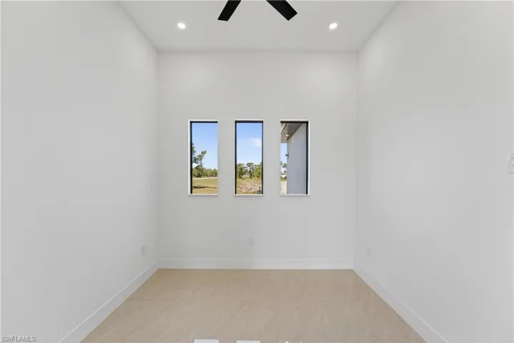 Bright interior space featuring three vertical windows, recessed lighting, a ceiling fan, light tile flooring, and white baseboards