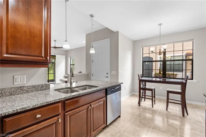 Kitchen featuring stainless steel dishwasher, light tile patterned floors, a sink, light stone countertops, and a chandelier