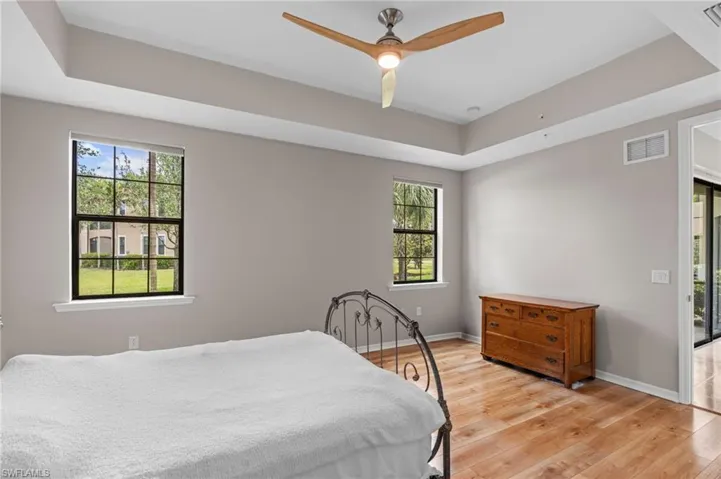 Bedroom featuring light wood-style floors, visible vents, a raised ceiling, and multiple windows