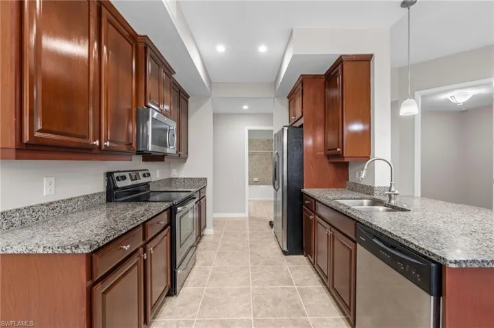 Kitchen with light tile patterned flooring, dark stone countertops, stainless steel appliances, and a sink