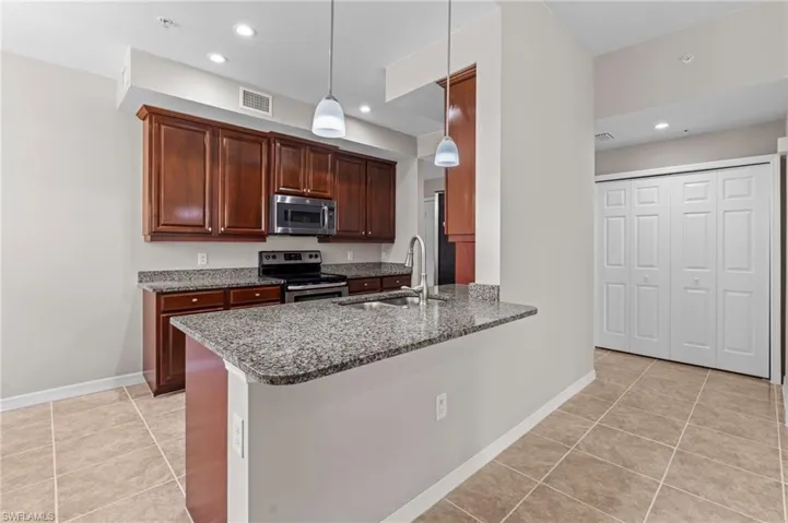 Kitchen featuring a sink, light tile patterned flooring, stone countertops, appliances with stainless steel finishes, and visible vents