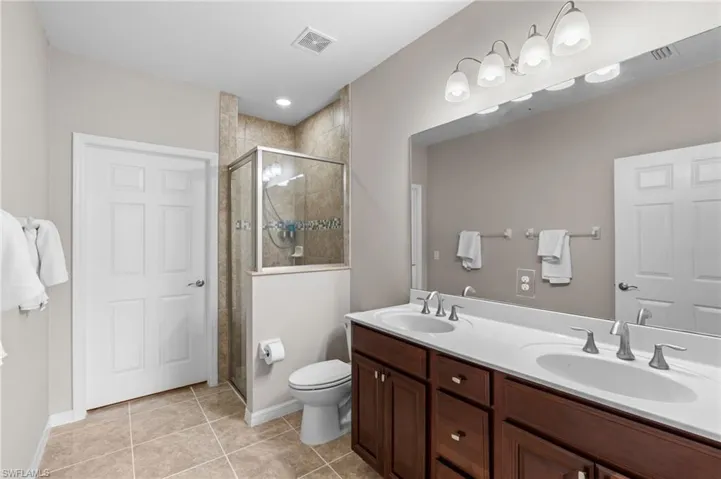 Full bathroom with a shower stall, toilet, a sink, and visible vents