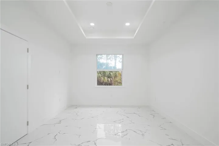 Empty room with a tray ceiling, light marble finish flooring, and recessed lighting
