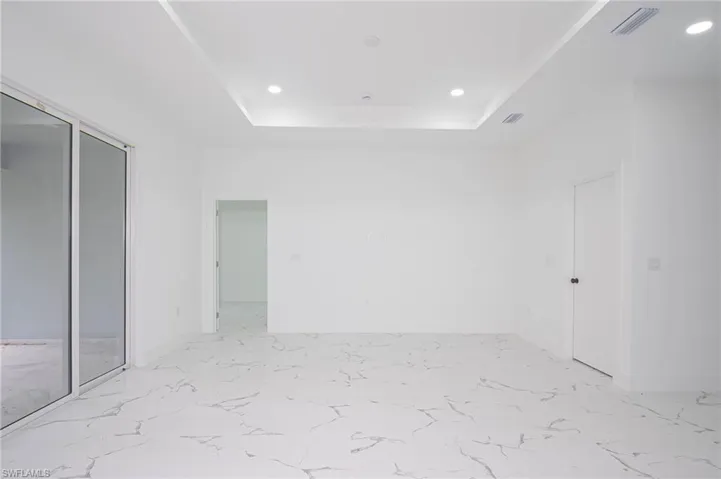Unfurnished bedroom featuring a tray ceiling, recessed lighting, and light marble finish floors