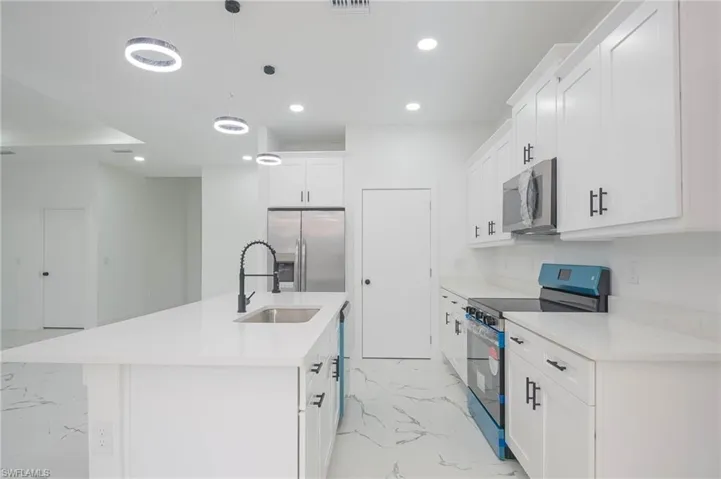 Kitchen featuring stainless steel appliances, light marble finish flooring, white cabinets, recessed lighting, and an island with sink