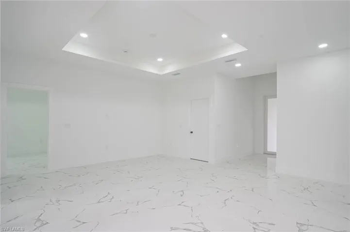 Empty room with recessed lighting, a tray ceiling, and light marble finish floors