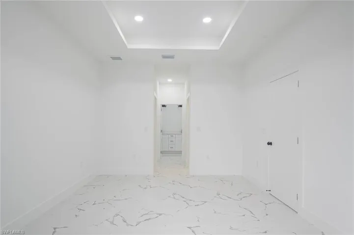 Spare room with recessed lighting, a raised ceiling, and light marble finish floors