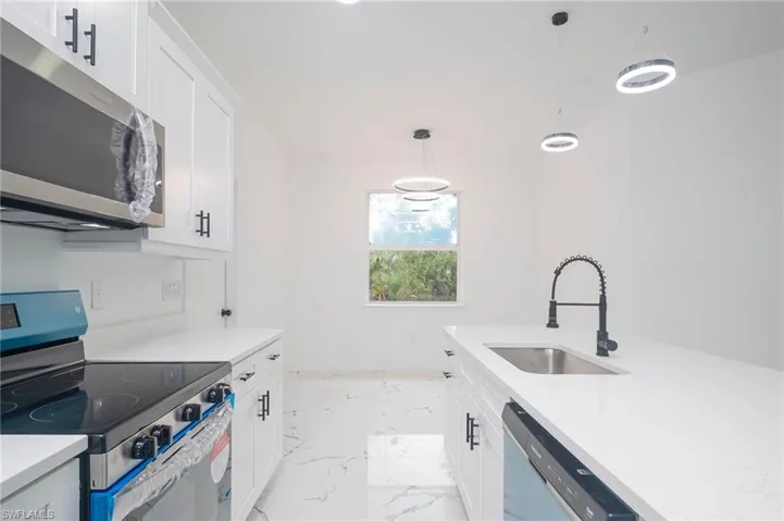 Kitchen featuring stainless steel appliances, light marble finish floors, pendant lighting, light countertops, and white cabinetry
