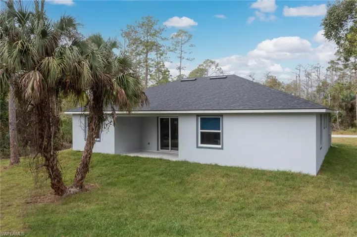 Back of property featuring roof with shingles, a patio, stucco siding, and a yard